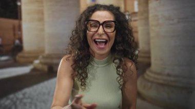 Kolsuz bir üst kolda gözlük takan kadın tarihi bir binanın yakınındaki kaldırımlı bir sokakta el çırpıyor..