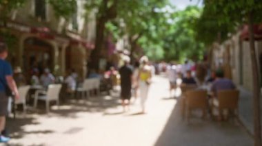 Kafe müşterileri, ağaçlarla dolu ve bulanık insanların yürüdüğü Mallorca 'nın güneşli bir sokağında yemek yemekten hoşlanırlar.