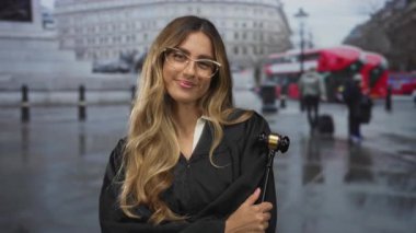 Kadın yargıç tokmak tutuyor ve kırmızı otobüs ve şehir meydanındaki yolcular arasında gülümsüyor; adalet otoritesi.