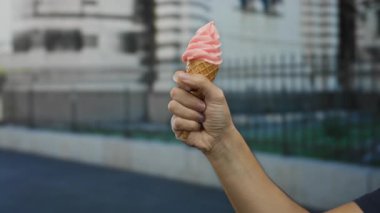 Şehir caddesinde elinde dondurma külahı tutan bir adam. Bulanık bir şehir arka planında doğal ışıkla yakalanmış..