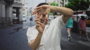 Beyaz gömlekli İspanyol adam, elleri ile kalp çerçevesini çerçeveler yoğun bir şehir caddesinde gün ışığında; sevgi.