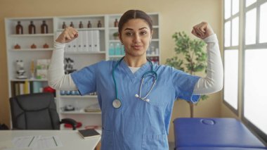 İspanyol kadın doktor bir hastane odasında kollarını rahatça esnetiyor, tıbbi bir iş yerinde güç ve profesyonellik gösteriyor..