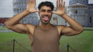 Kahverengi kolsuz tişörtlü adam orta parmak hareketini Pisa kulesinde gösteriyor..