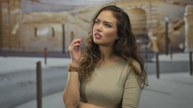 Güneşli bir günde arka planda antik mimari ve arabalarla çevrili, düşünceli bir ifadeyle, eski bir kasabada açık havada düşünen bir kadın..