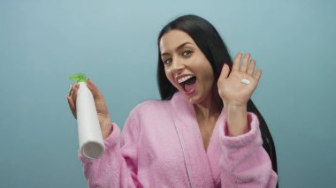 Pembe bornozlu İspanyol kadın mavi bir arka plana karşı coşkuyla cilt losyonu tutuyor..