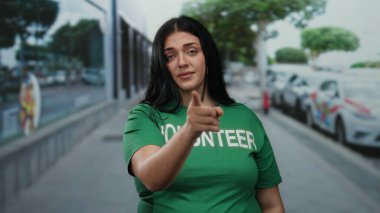 Şehir caddesinde yeşil tişörtlü, şehir merkezini gösteren jest yapan gönüllü bir kadın.