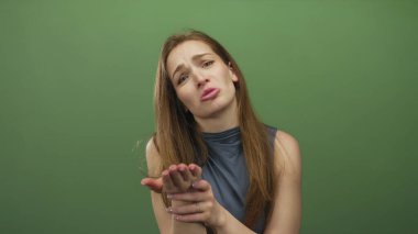 Avuç içi açık yalvaran ve yeşil stüdyo ortamında yüz ifadesini savunan beyaz bir kadın, çaresizlik savunması..