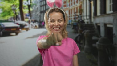 Tavşan kulağı takan pembe tişörtlü genç sarışın kadın kaldırım taşı sokağındaki tümsek için yumruğunu uzatıyor..