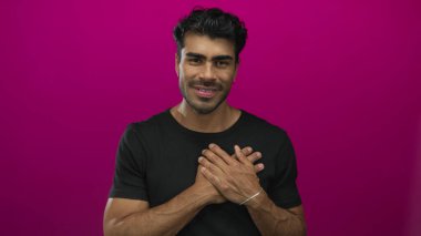 Mor renkli stüdyo resmi ile göğsünü tutan siyah tişörtlü bir adam hafif ışıklandırma altında; minnettarlık.