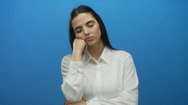 Beyaz gömlekli, mavi bir duvara yaslanan kadın bıkkınlık ve bıkkınlık gösteriyor..