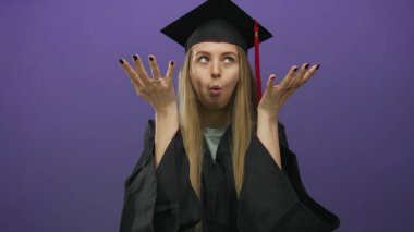 Mezuniyet şapkalı ve cüppeli genç bir kadın canlı mor bir arka plana karşı neşeli bir bakışla anlamlı jestler yapıyor..