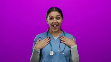 Mavi önlüklü, steteskoplu İspanyol hemşire, kendini izole edilmiş pembe duvar arka planına işaret ederek şaşırmış görünüyor..