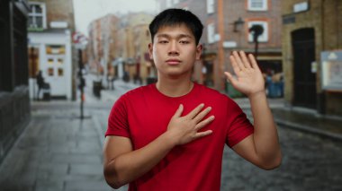 Şehir sokaklarında kırmızı gömlekli genç adam, şehir mimarisi ve kaldırım kaldırımlarının bir zeminine karşı duygularını ifade ederek, hareketli bir açık hava sahnesi yakalıyor..