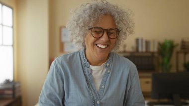 Kitaplıklar ve bitkilerle dolu parlak bir ofis odasında neşeyle gülen bir kadın iş yerinde bir anlık mutluluğu yakalıyor..