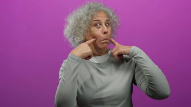 Kıvırcık gri saçlı kadın canlı pembe bir duvara karşı neşeli yüzler sergiliyor ve enerjiyi ve duyguları yakalıyor..