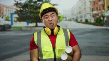 Şehir caddesinde inşaat malzemesi giymiş genç bir adam eğlenceli bir inşaat sahnesi öneriyor..