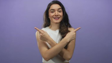 Genç kadın parmaklarını göstererek stüdyoda mor arka planda çıplak kollarını ve beyaz ekin üstünü gösteriyor; mutluluk..