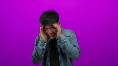 Gülümseyen genç adam ellerini pembe arka plana doğru uzatarak neşeli bir şekilde gülümsüyor. Kot ceket giyiyor ve neşe saçıyor..