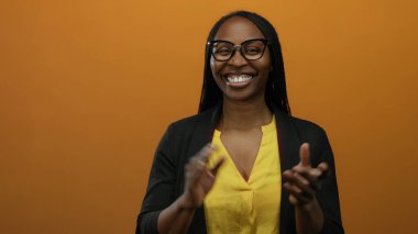 Sarı bluz ve gözlük takmış, turuncu arka planda el çırpan kadın, izole edilmiş sıcak bir ortam ve canlı bir ortam ile neşeli bir ifade sergiliyor..