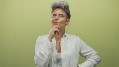 Kadın, profesyonel stüdyoda yumuşak yeşil zemin ile düşünceli pozda çeneye dokunur; merak içgözlem.