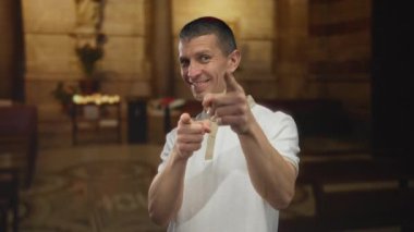 Kafkasyalı bir adam kilisede gülümsüyor ve içeriyi işaret ediyor. Arkasında taş duvarlar olan canlı bir atmosfer yakalıyor..