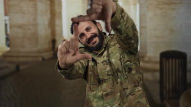 Askeri üniformalı İspanyol bir adam, eski Roma şehir ortamında gülümseyen elleriyle manzara çerçevesi çiziyor, hikaye anlatma ya da fotoğrafçılık öneriyor..