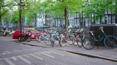 Amsterdam 'da arka planda ağaçlar ve binalar bulunan bulanık bisiklet ve kanallar, Hollanda' daki şehir hayatının özünü yakalıyor..