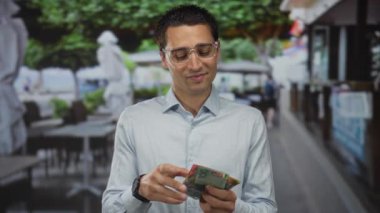 Rahat bir kafeterya terasında Avustralya doları tutan genç bir adam, rahat bir anda tatmin ve rahatlık hissi veriyor..