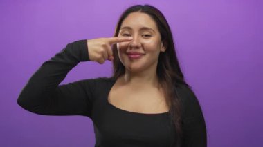 Stüdyoda siyah bir üst parmak ile mor bir duvara yaslanan Latin kökenli genç bir kadın..