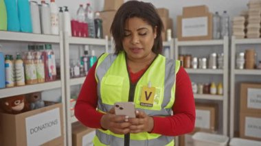 Yansıtıcı yelek giyen gönüllü bir kadın telefonunu bir hayır kurumunun bağış merkezinde kullanıyor..