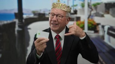 Takım elbiseli kıdemli bir adam deniz kenarındaki gezinti alanında kart tutuyor. Açık havada kendine güvenen, eğlenceli bir iş teması öneriyor..