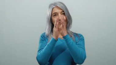 Mavi tişörtlü yaşlı bir kadın izole edilmiş beyaz bir arka plana karşı el ele dua ederek huzur ve bilgeliği temsil eden huzur ve maneviyatı yayıyor..