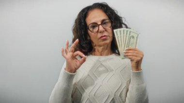 Elinde dolar banknotları olan orta yaşlı bir kadın izole edilmiş beyaz bir geçmişe karşı iyi bir jest yapıyor. Finansal güven ve başarı tasvir ediyor..