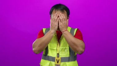 Gönüllü nişanlı sarı yelek giyen Asyalı bir adam tecrit edilmiş pembe bir duvarın karşısında duruyor..