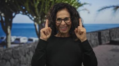 Kadın işaret parmağını okyanus kıyısındaki gezinti güvertesinde yukarı kaldırıyor; iyimserlik umut pozitifliği esin kaynağı.