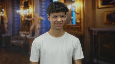 Gözlüklü genç adam tarihi galeri binasında mermer heykelin yanında burun büküyor..