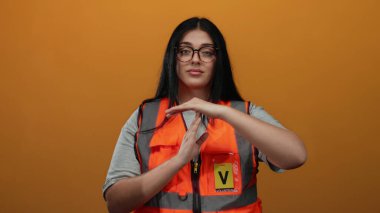 Turuncu arka planda güvenlik yeleği giyip izole iletişim tasvir eden gönüllü bir kadın..