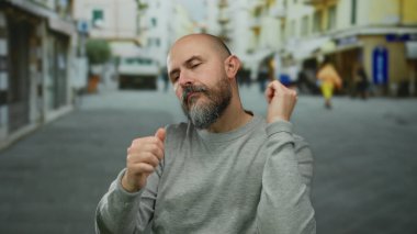 Kel ve sakallı bir adam gün boyunca şehir sokaklarında enerjik bir şekilde dans ediyor, kaygısız bir ruh ve kendine güvenen hareketler sergiliyor, günlük gri süveter giyiyor, şehir planıyla harmanlanıyor..