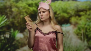 Pembe gece elbisesi ve tavşan maskesi takan, elinde ağaçlarla tarak tutan, duygularını ifade eden bir kadın..