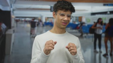 Gözlüklü bir adam havaalanı terminalinde masa başında yumruklarını sıkar ve gözleri görür bir şekilde şaşı kesilir..