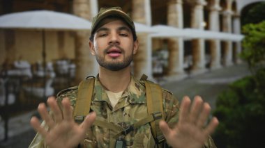 Kamuflaj üniformalı genç İspanyol adam binanın önünde görünür künyelerle el ele tutuşuyor..
