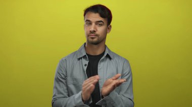 İspanyol adam, izole edilmiş sarı arka planda el çırpıyor. Günlük kıyafetler giyiyor ve anlamlı bir görünüm sergiliyor..