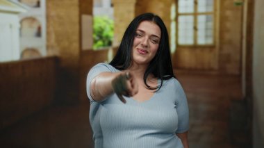 Yaşlı bir üniversitenin kapalı koridorunu gösteren, kendine güvenen, tarihi mimariyle çevrili, açık mavi bluzlu genç bir kadın..