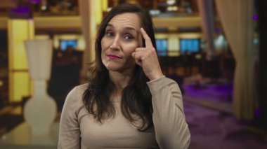 Latin kökenli genç bir kadın şık bir otel odasında, oturma alanının yakınını işaret ediyor..