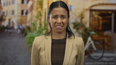 Yüzünde hoşnutsuzluk ifadesi olan bir kadın, arka plandaki tarihi mimariyle çelişen kentsel rahatsızlığı canlandırarak eski şehir caddesinde duruyor.