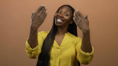 Güvenle gülümseyen kadın, kahverengi arka planda sarı gömlekli kameraya bakıyor. Neşeli bir ifade sergiliyor..