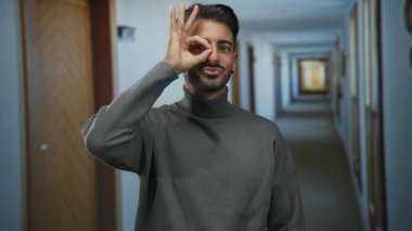 İnsan otel koridorunda gri balıkçı yaka kazak giyerek el dürbünüyle gözü çerçeveler; merak.