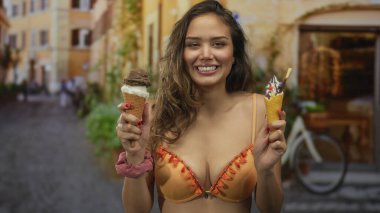 Açık bir sokak ortamında elinde dondurma külahıyla gülümseyen bir kadın bikini giyiyor ve kentsel bir çevre ile çevrili neşeli bir an yaşıyor..