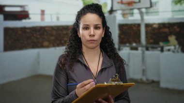 Açık hava basketbol sahasındaki panoya notlar yazan kadın odaklanmış ifade, kararlılık ve odaklanmayı vurguluyor.