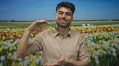 Gözlük takan adam, ormanda canlı çiçekler üzerinde gülümseyen yüzle el ele tutuşuyor; büyüme bolluğu sevinci.